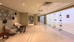 Eine Hotelhalle mit Sitzgelegenheit, einer Rezeption und einer Glastrennwand mit nummerierten Zimmern.
