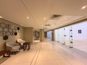 Eine Hotelhalle mit Sitzgelegenheit, einer Rezeption und einer Glastrennwand mit nummerierten Zimmern.