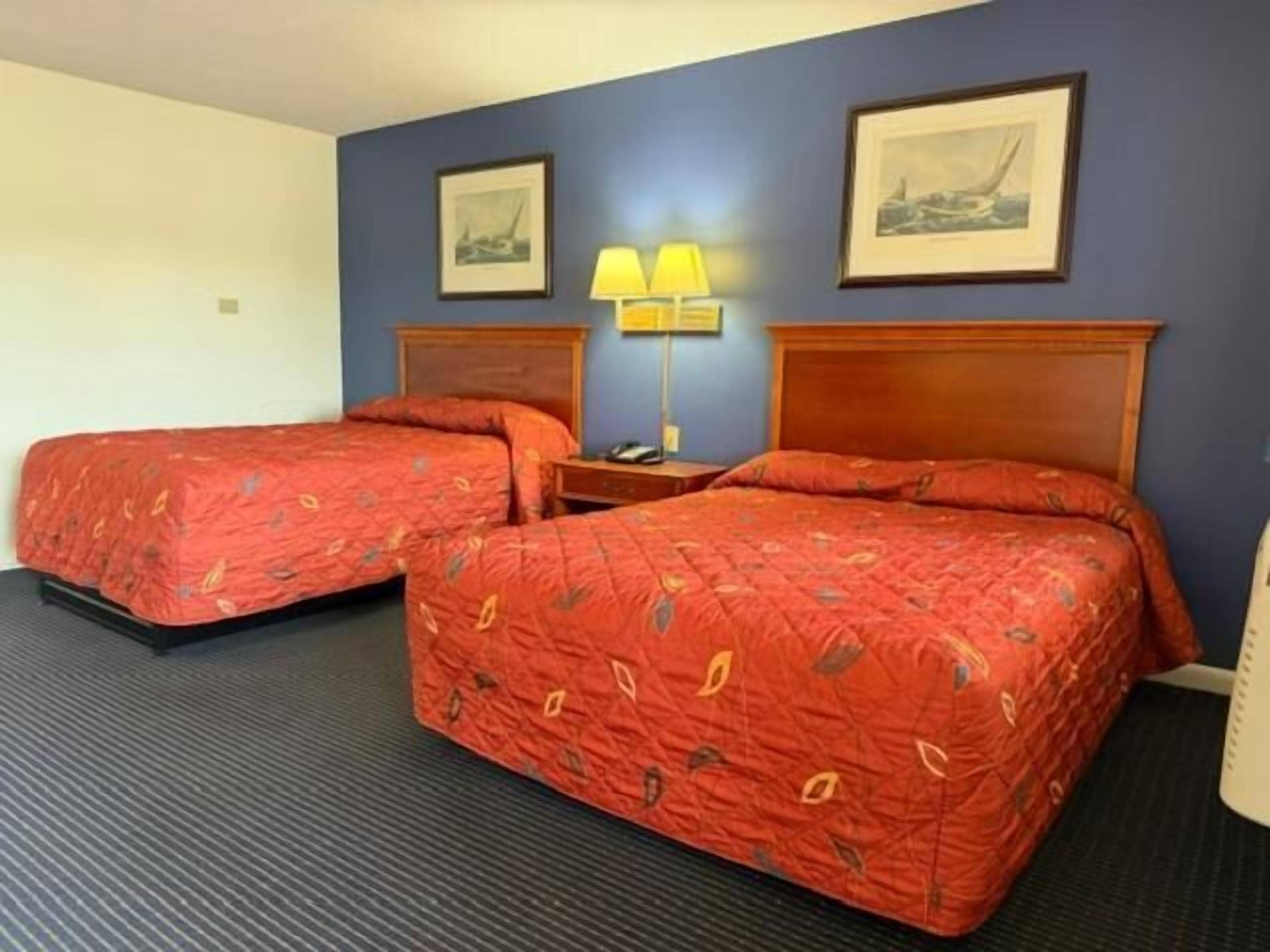Et hotelværelse med to senge, et natbord med en lampe og to billeder i rammer på væggen.