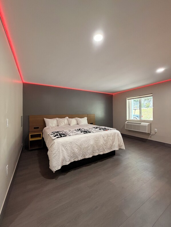 A bedroom with a bed, bedside table, and a window with an air conditioning unit. - Wethersfield Motel (Wethersfield)