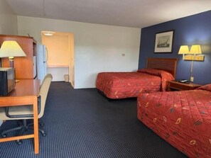 A hotel room with a desk, two beds, a chair, a lamp, and a picture on the wall.
