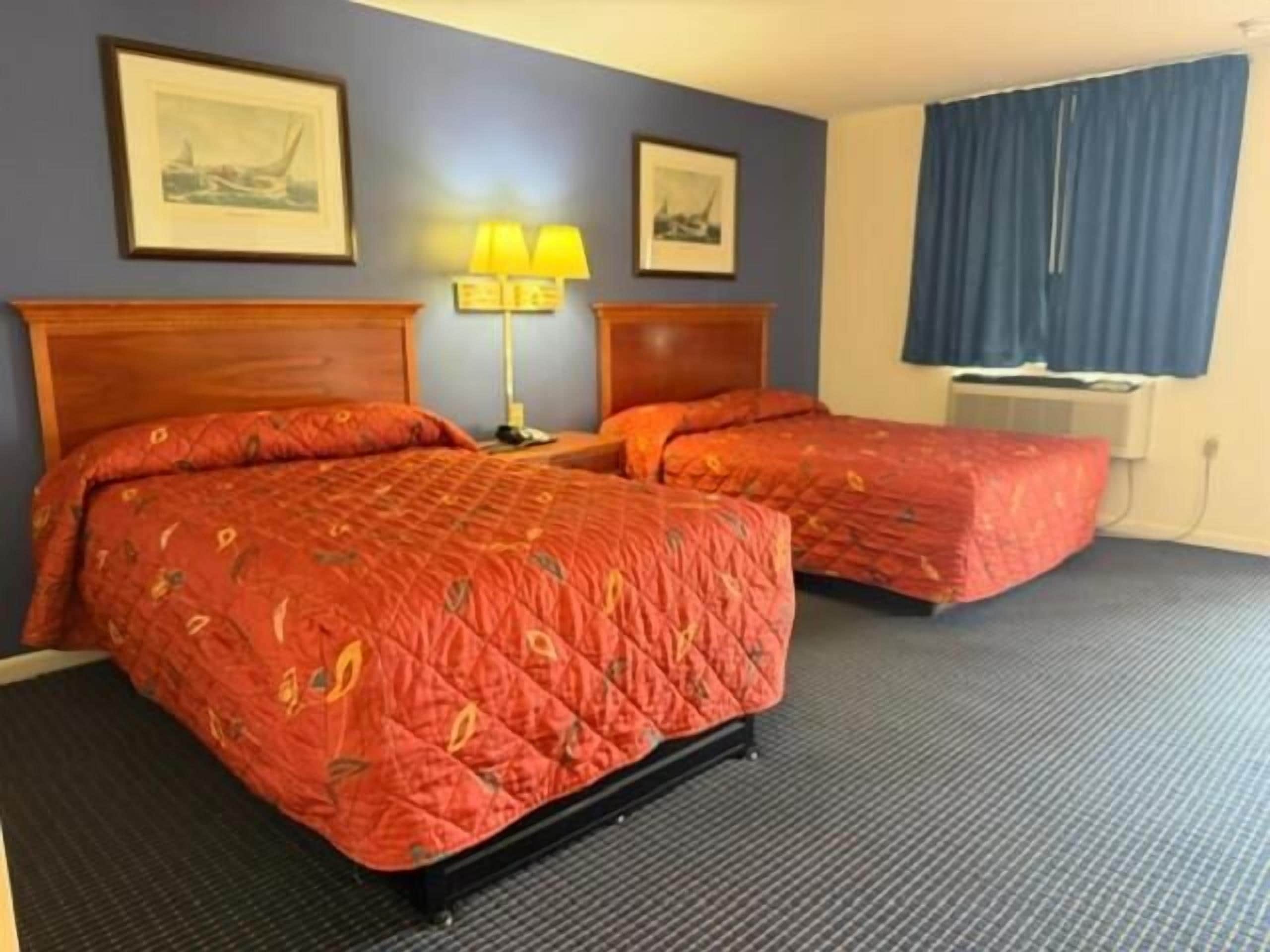 A hotel room with two beds, a lamp, and a window with curtains.