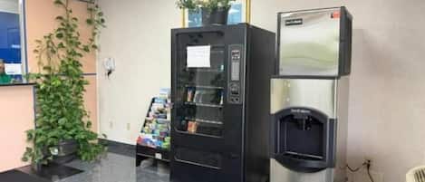 A vending machine and a water dispenser in a public area with a tiled floor and a potted plant.