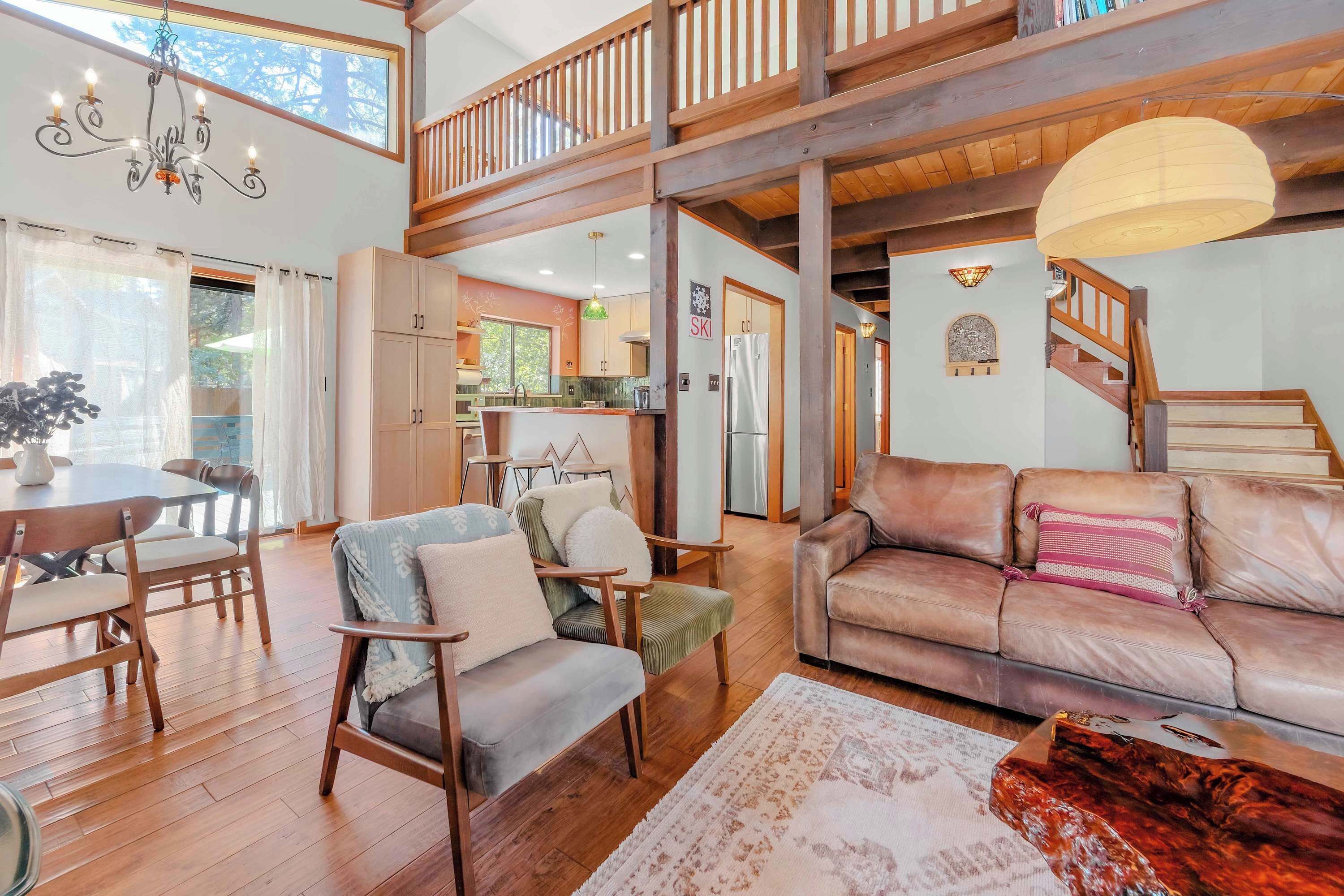A spacious living area with a high ceiling, wooden flooring, a dining set, and a cozy seating area with a leather sofa and armchairs.
