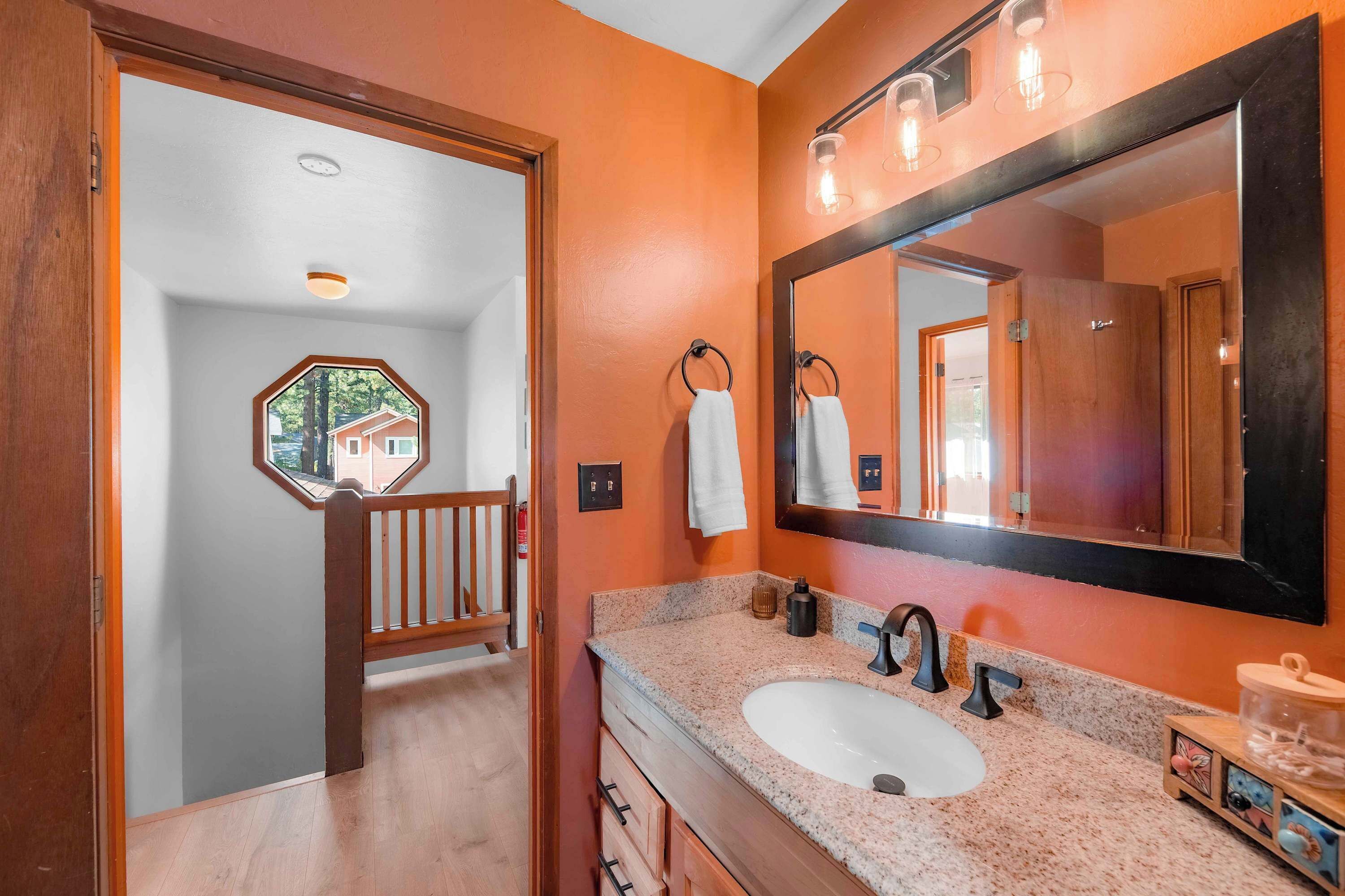 Une salle de bain avec un grand miroir, un lavabo et une porte en bois donnant sur un couloir.