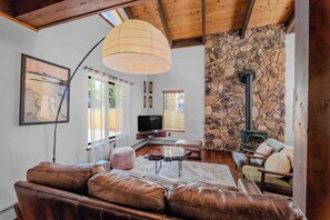 A cozy living room with a stone wall, a fireplace, leather sofas, and a television.