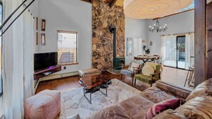 A spacious living room with a stone wall, a fireplace, a television, and a dining area with chairs and a table. - Lakewood Escape 3BR Retreat (South Lake Tahoe)