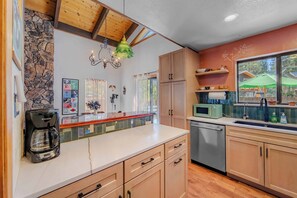 A kitchen with wooden cabinets, a stone wall, a coffee maker, and a microwave. - Lakewood Escape 3BR Retreat (South Lake Tahoe)