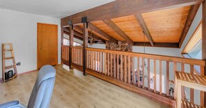 Ein Zimmer mit Holzbalkendecke, Steinwand, Holzgeländer und einer Tür.