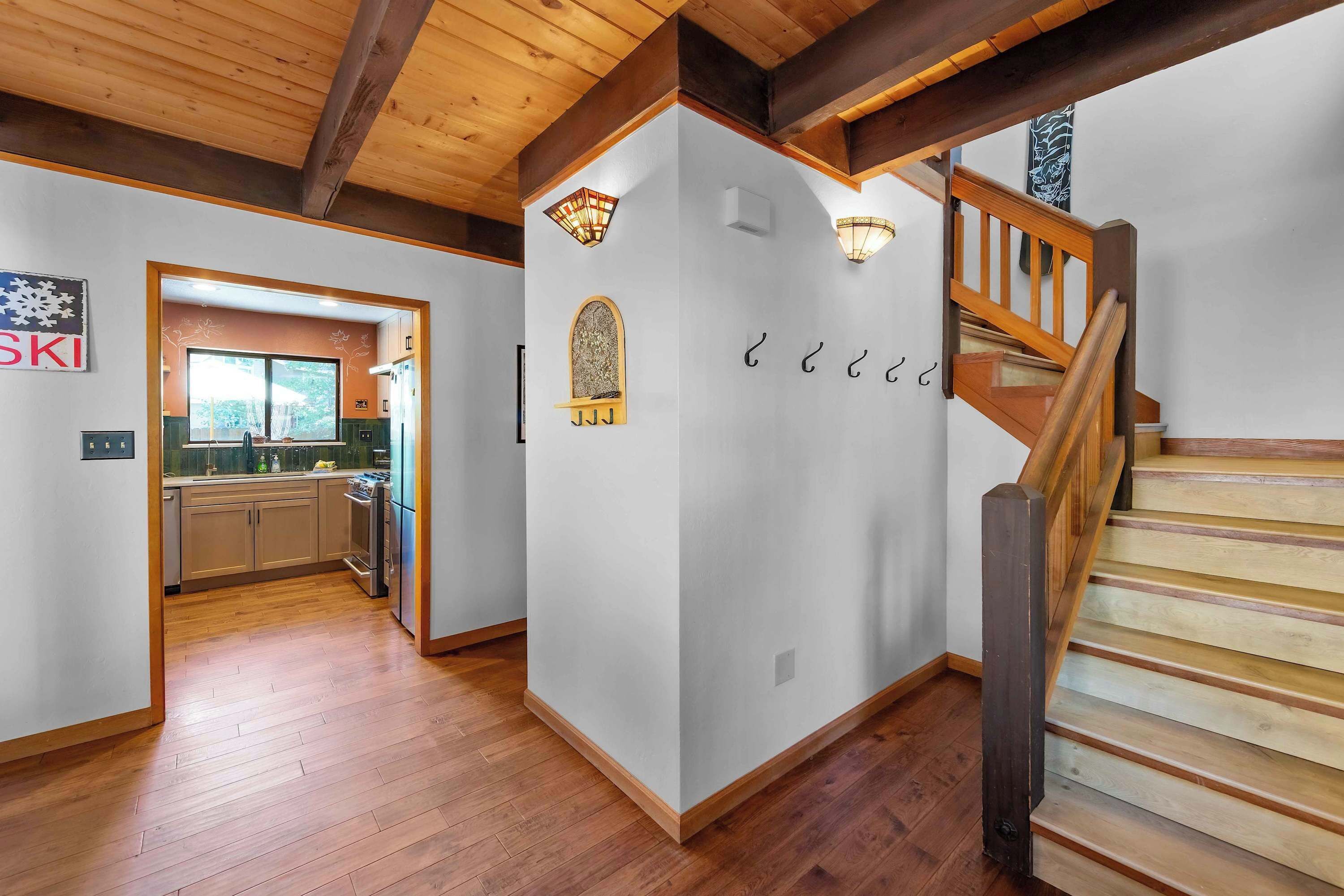 A modern interior with a wooden staircase, a kitchen with a large window, and a wall-mounted light fixture.
