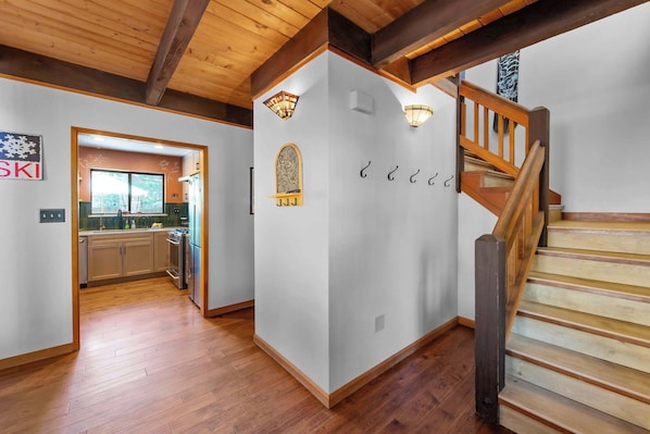 A modern interior with a wooden staircase, a kitchen with a large window, and a wall-mounted light fixture.