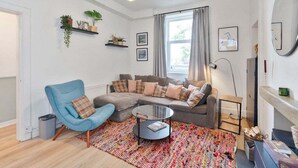 A living room with a blue armchair, a grey sectional sofa, a round coffee table, and a patterned rug. - GuestReady - Charming 1Bed near Edinburgh Beach (Edinburgh)