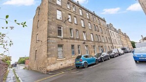 A multi-story building with a row of parked cars along the street. - GuestReady - Charming 1Bed near Edinburgh Beach (Edinburgh)