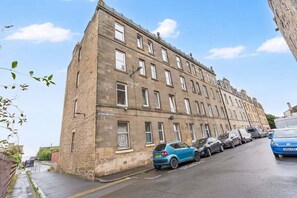 A multi-story building with a row of parked cars along the street. - GuestReady - Charming 1Bed near Edinburgh Beach (Edinburgh)