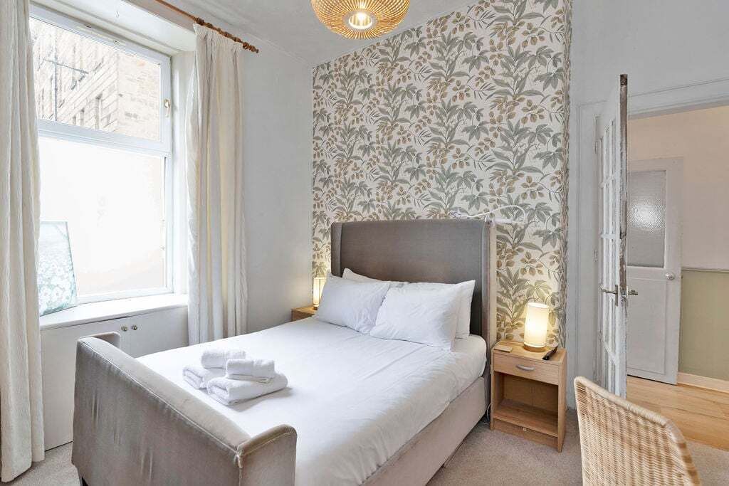 Une chambre d’hôtel avec un grand lit, une table de chevet avec une lampe, une fenêtre avec des rideaux et une porte.