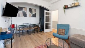 A modern living room with a dining area, a flat-screen TV mounted on the wall, and a blue armchair. - GuestReady - Charming 1Bed near Edinburgh Beach (Edinburgh)