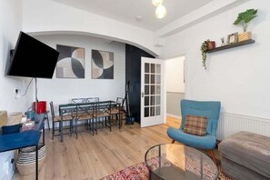 A modern living room with a dining area, a flat-screen TV mounted on the wall, and a blue armchair. - GuestReady - Charming 1Bed near Edinburgh Beach (Edinburgh)