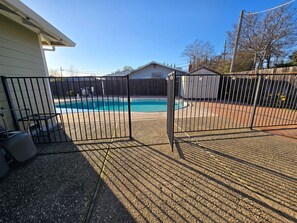 A backyard with a swimming pool, a fenced area, and a house.