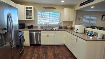 A modern kitchen with stainless steel appliances, white cabinetry, and a wooden floor.