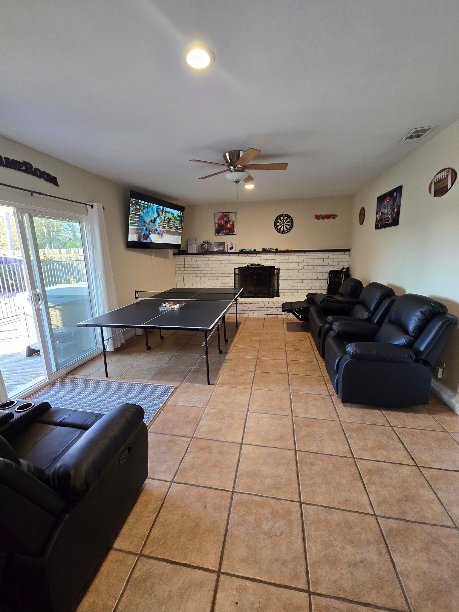 Una sala de estar con mesa de ping pong, sofá de cuero negro y chimenea.