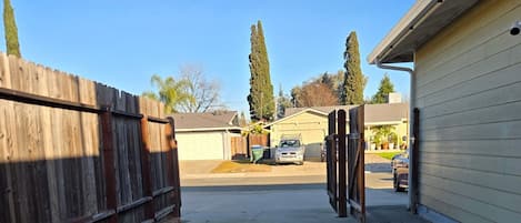 Uma entrada de concreto que leva a uma garagem, com uma cerca de madeira de um lado e um edifício do outro.