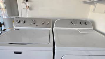 Une buanderie équipée de deux machines à laver à chargement frontal, de couleur blanche, d’une étagère contenant des produits de nettoyage et d’une prise électrique murale.