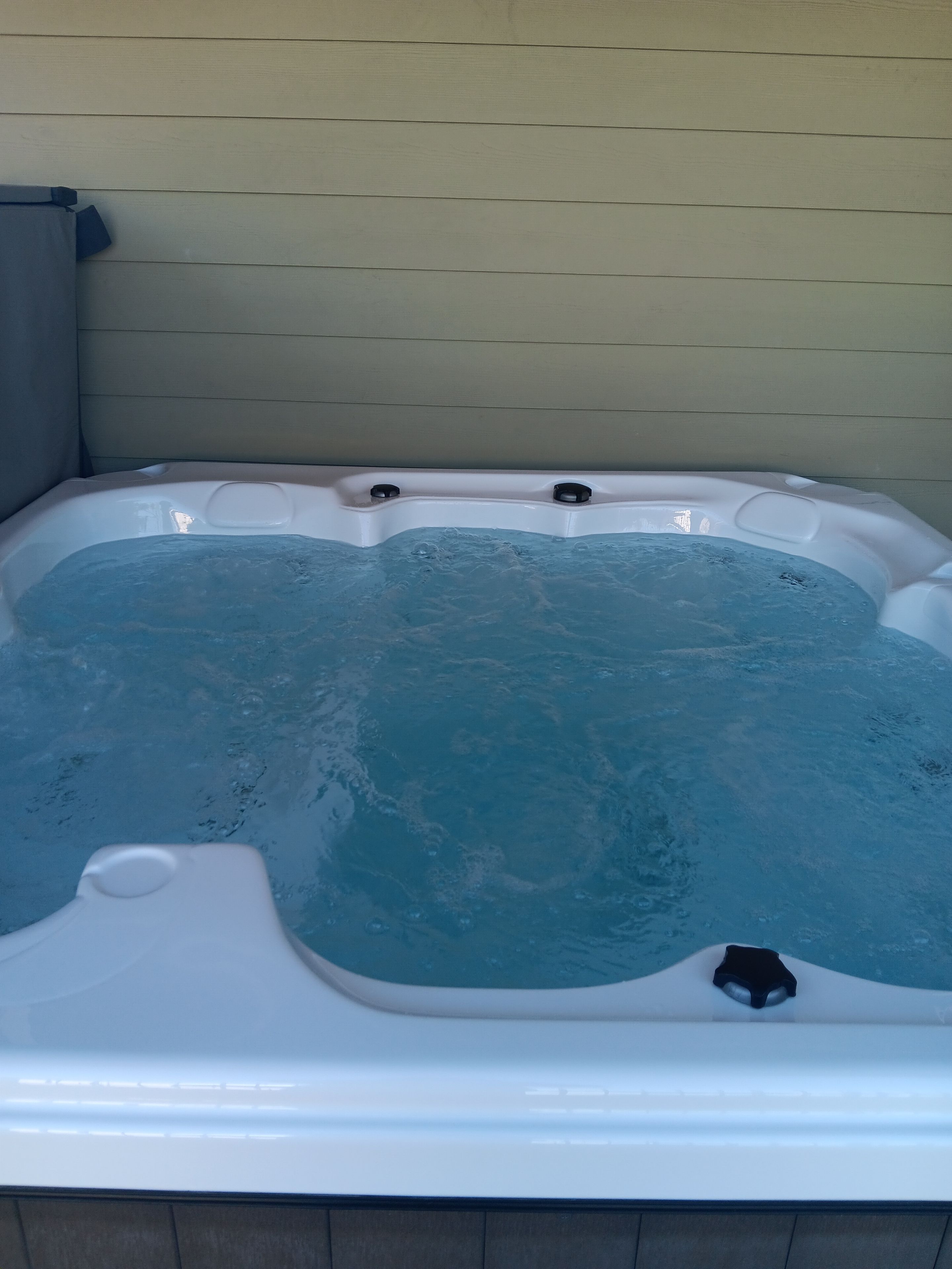 Un jacuzzi con revestimiento blanco y parte interior azul, frente a una pared de color claro.