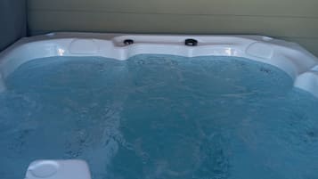 A hot tub with a white exterior and a blue interior, set against a light-colored wall.