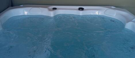 Un jacuzzi con revestimiento blanco y parte interior azul, frente a una pared de color claro.