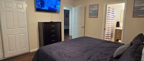 Un dormitorio con cama, ventilador de techo, televisor montado en la pared y cómoda.