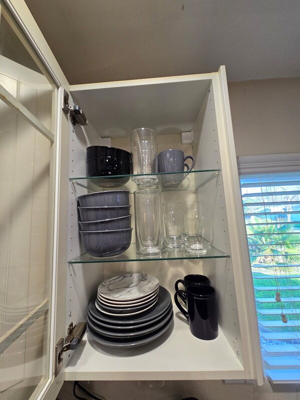 A kitchen cabinet with shelves containing plates, bowls, glasses, and a pitcher.