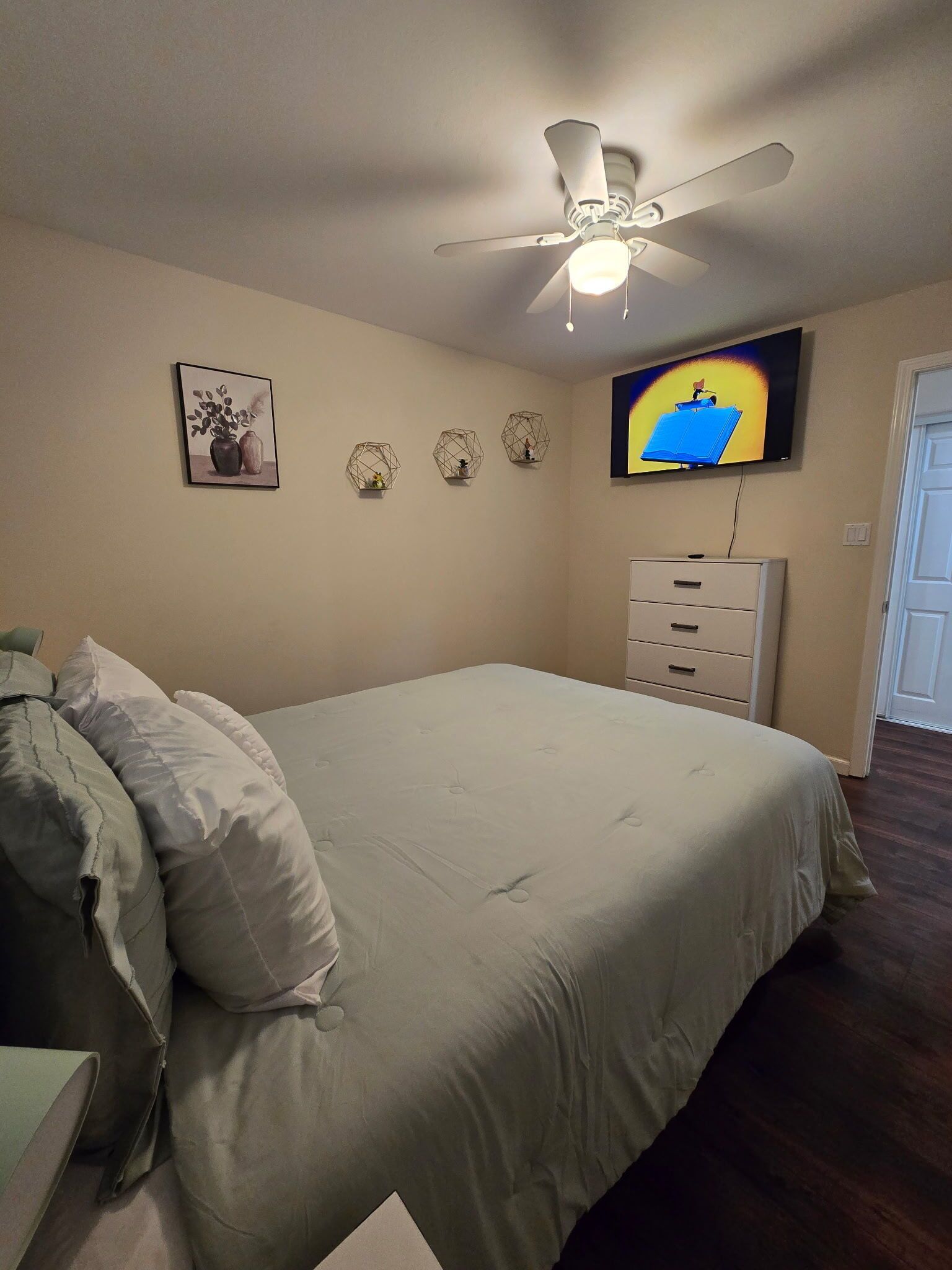A bedroom with a bed, a ceiling fan, a television, and a dresser.