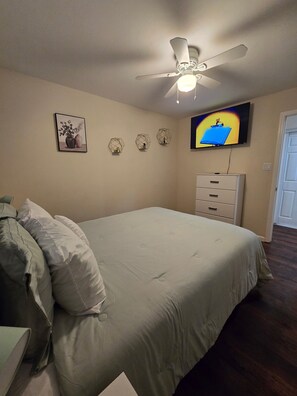 A bedroom with a bed, a ceiling fan, a television, and a dresser.