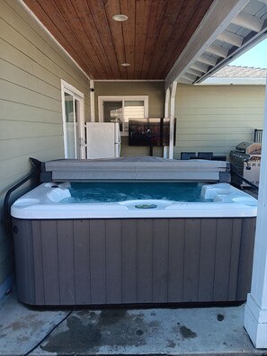 A hot tub with a wooden deck, a television, and a grill in the background.