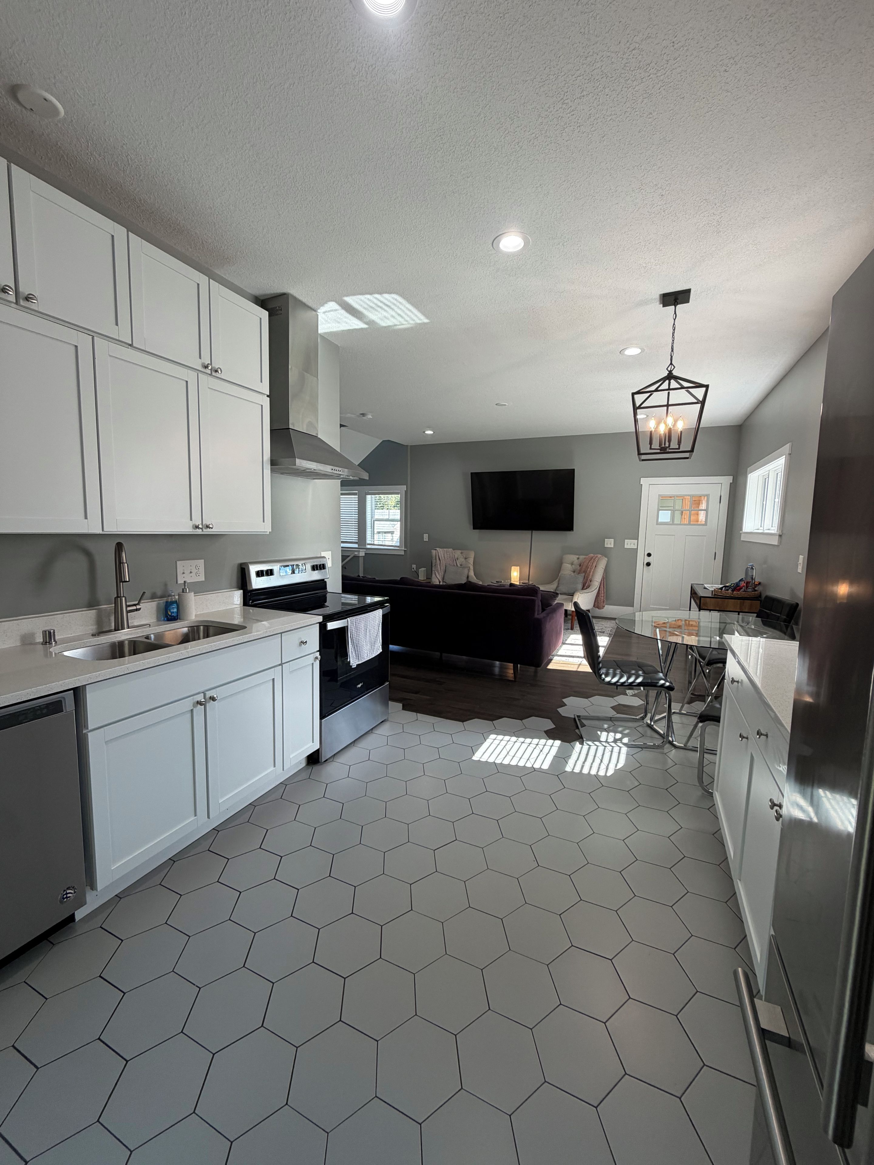 A modern kitchen with white cabinets, a black stove, and a hexagonal tile floor.