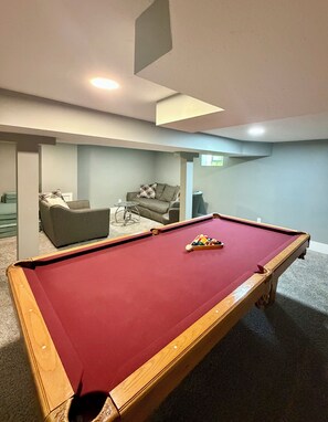 A pool table with balls in the center, a sofa, and a chair in a room with light-colored walls and carpet. - 3 King Beds Minnehaha Hideaway Near Downtown (Minneapolis)
