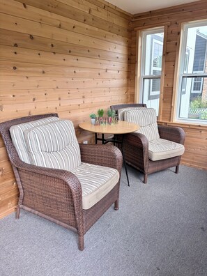 A room with wooden panel walls, two wicker chairs with striped cushions, a small round table, and a window with a view of a house. - 3 King Beds Minnehaha Hideaway Near Downtown (Minneapolis)
