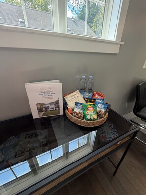 Ein Glastisch mit einer Willkommensmappe, Wasserflaschen, Snacks und einer Korb voller Kekse.