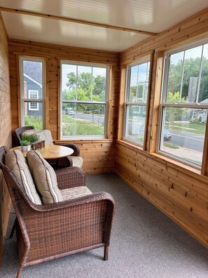 A corner room with a wicker sofa, a small table, and large windows offering a view of a residential street. - 3 King Beds Minnehaha Hideaway Near Downtown (Minneapolis)