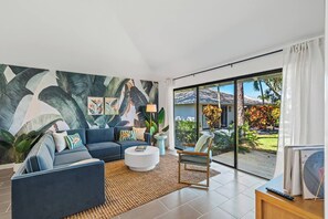 Un salon moderne avec un canapé bleu, une table basse blanche et une grande porte vitrée donnant sur un jardin.
