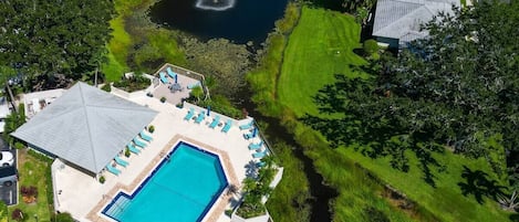 Ein Swimmingpool mit Liegestühlen und einer Fontäne, umgeben von gepflegten Rasenflächen und Bäumen.