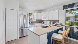 A modern kitchen with white cabinetry, stainless steel appliances, a granite countertop, and a large island with seating. - PGA Resort Home – Heated Pool, Walk to Dining & 15 min Drive to Beaches (Palm Beach Gardens)