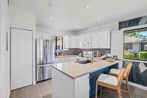 A modern kitchen with white cabinetry, stainless steel appliances, a granite countertop, and a large island with seating. - PGA Resort Home – Heated Pool, Walk to Dining & 15 min Drive to Beaches (Palm Beach Gardens)
