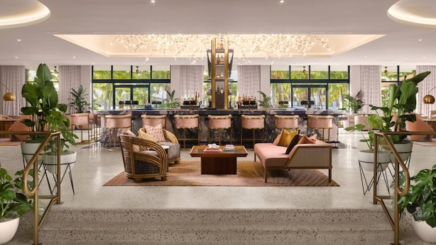 A spacious lounge area with a bar, comfortable seating, and large windows offering a view of greenery. - PGA Resort Home – Heated Pool, Walk to Dining & 15 min Drive to Beaches (Palm Beach Gardens)