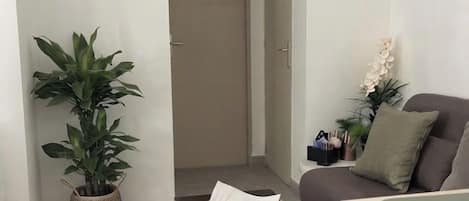 Una sala de estar con un sofá, una mesita de centro, una planta en maceta y una puerta que da a otra habitación.