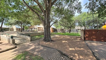 Un parque con zona de picnic, espacio de descanso cubierto y área de juegos cercada.