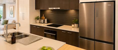 A modern kitchen with a stainless steel refrigerator, a built-in oven, and a sink with a cutting board.