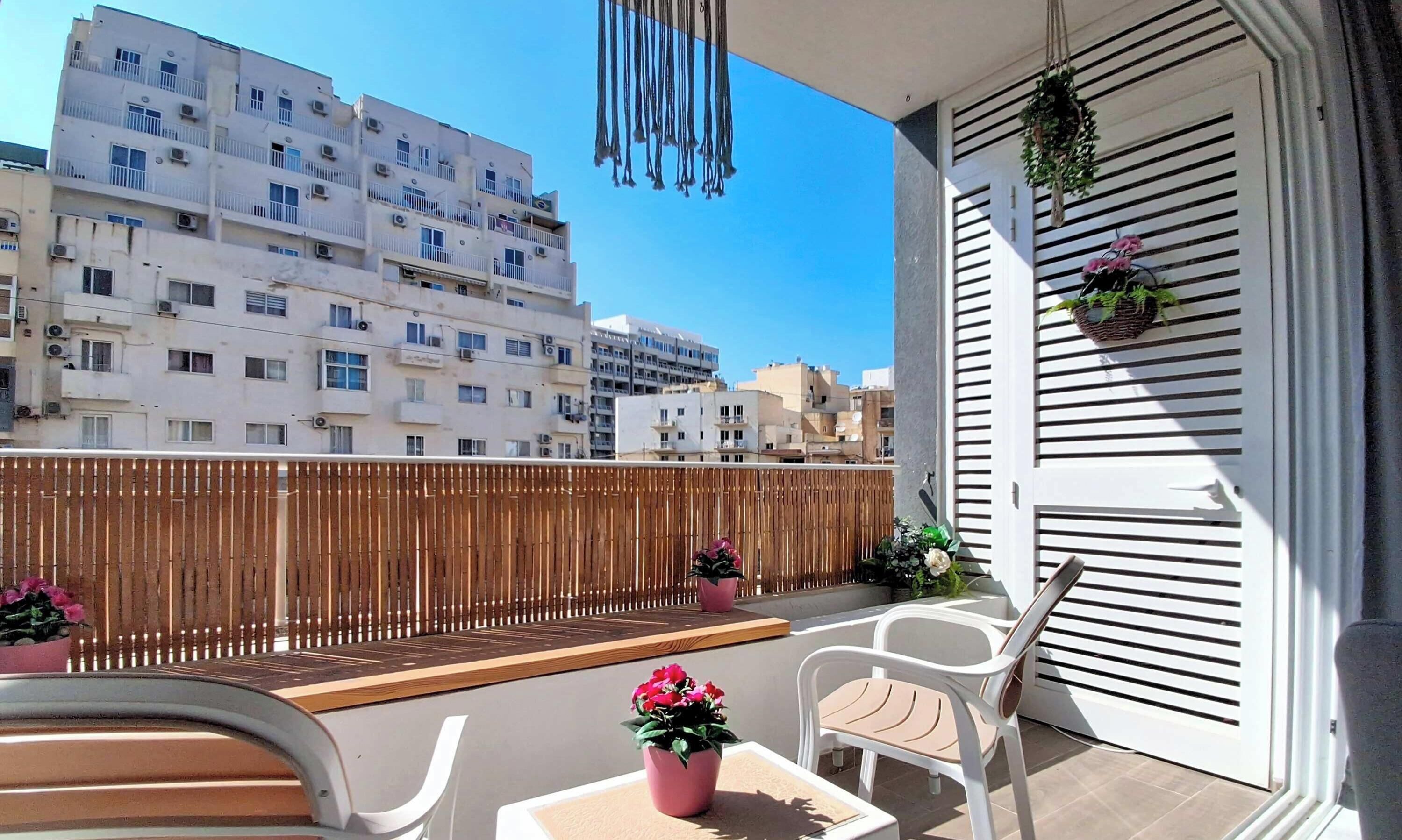 Ein Balkon mit Blick auf Wohnhäuser, einen Holzzaun und Kübelpflanzen.