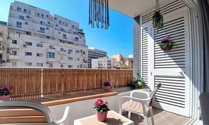 Un balcon donnant sur des immeubles d’habitation, avec une clôture en bois et des plantes en pot.