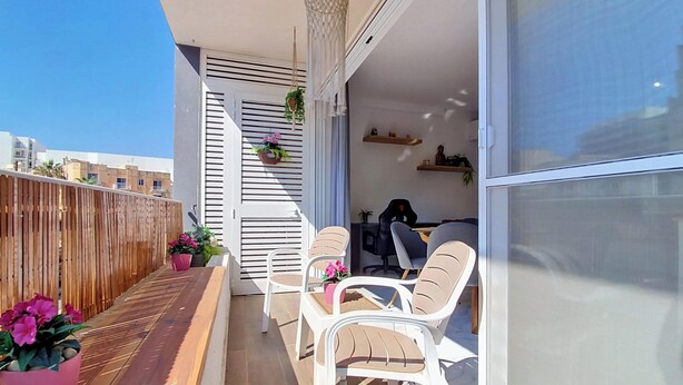 A balcony with a wooden floor, white chairs, and potted plants.
